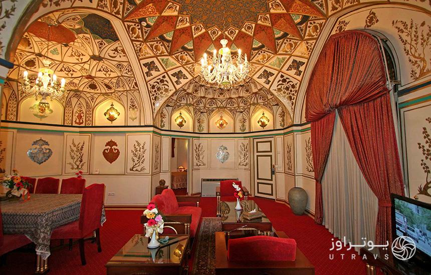 اتاقی در هتل «عباسی» اصفهان با معماری سنتی که موکت و صندلی‌های قرمزرنگ دارد با نقاشی‌هایی روی سقف و دیوارها